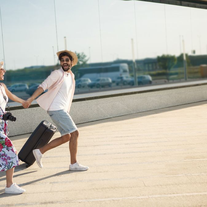 Ein Paar läuft mit Koffern aufgeregt einen Weg entlang