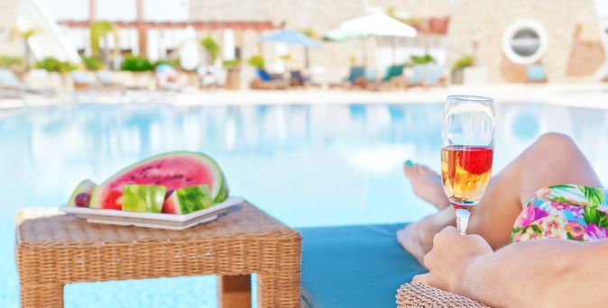 Person liegt am Pool mit Obst und Getränk
