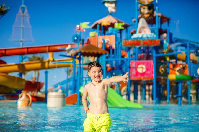Junge steht vor einem Aquapark und zeigt einen Daumen hoch