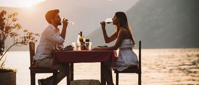 Eine Frau und ein Mann sitzen an einem Tisch am Wasser und trinken Wein