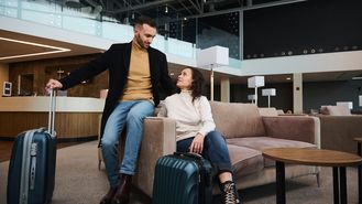 Eine Frau und ein Mann sitzen mit Koffern in einer Lobby und schauen sich an