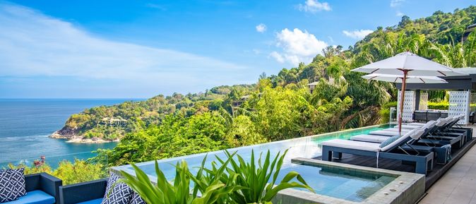 Ein eleganter Infinity Pool umgeben von Ledersofas, Liegen und Pflanzen mit Blick auf das Meer