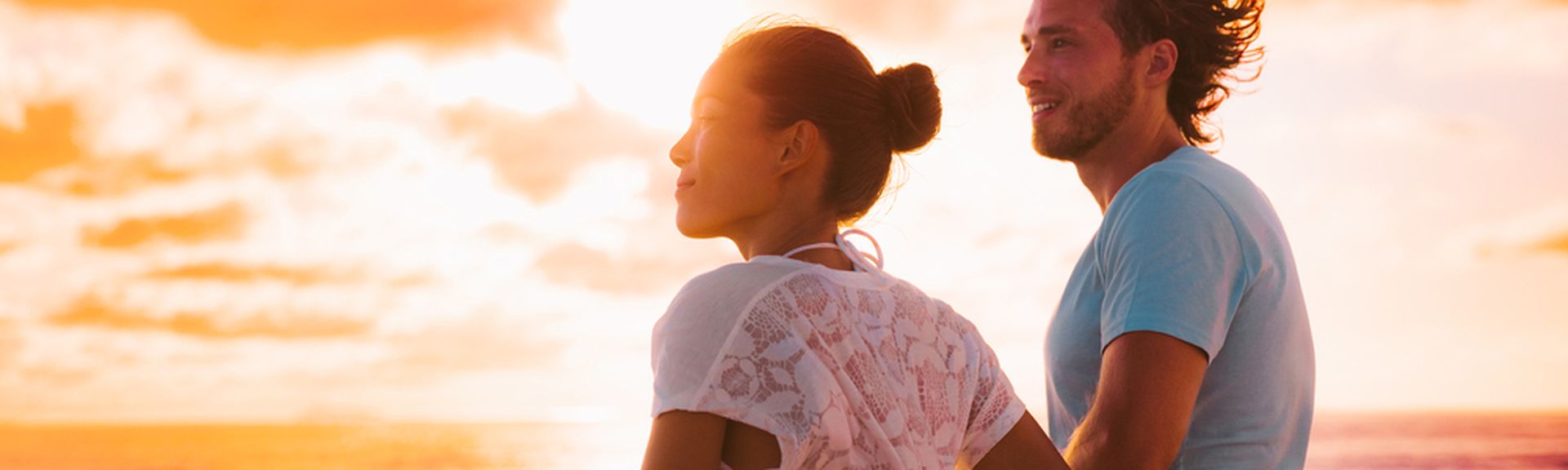 Eine Frau und ein Mann stehen bei Sonnenuntergang an der Reling eines Kreuzfahrtschiffes