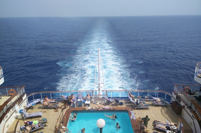 Im Pool am Heck eines Kreuzfahrtschiffes sieht man einige Urlauber schwimmen und sich sonnen