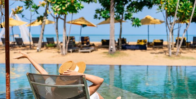 Frau sitzt auf einer Liege am Pool mit Strandzugang