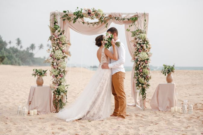 Ein Hochzeitspaar küsst sich unter einem Traubogen am Strand