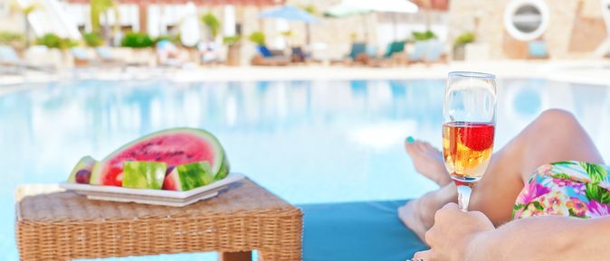 Person liegt am Pool mit Obst und Getränk