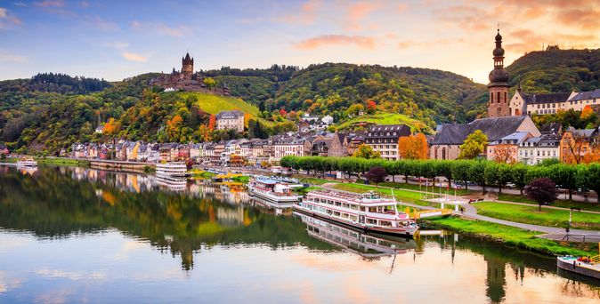 Schiffe am Ufer der Mosel mit Häusern und Sonnenuntergang im Hintergrund