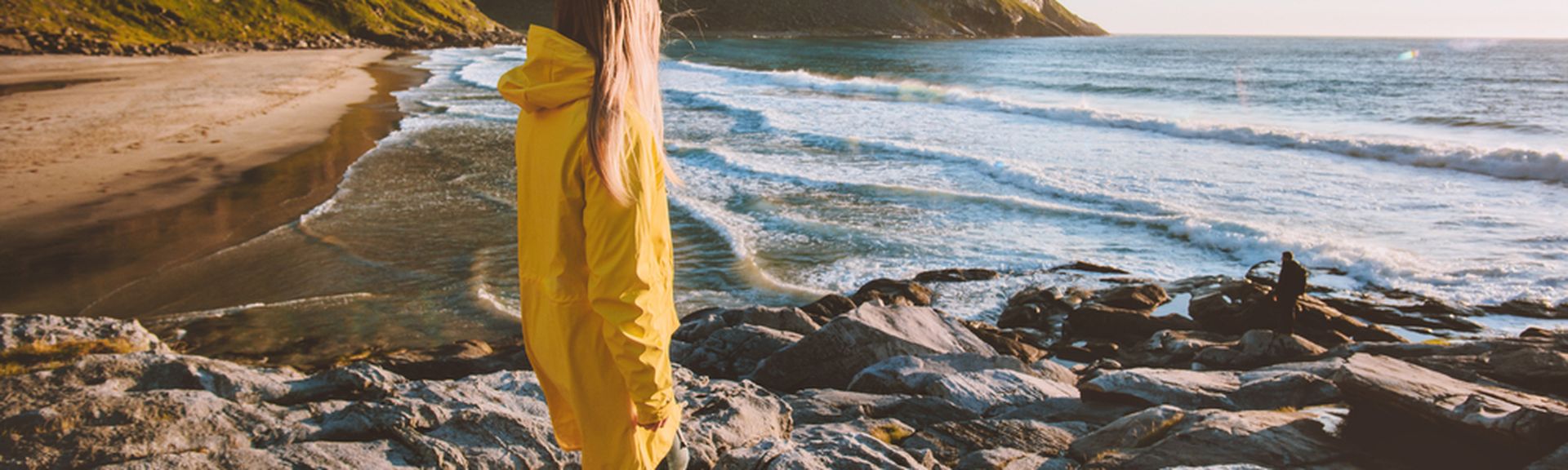 Eine Frau in einer gelben Regenjacke schaut auf das Meer