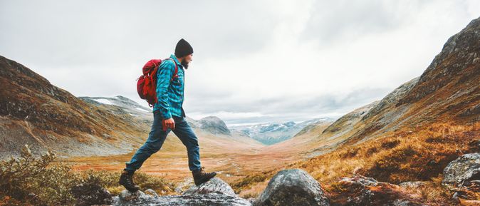 Ein Mann in Wanderkleidung läuft in einer Berglandschaft über Steine in einem Bach