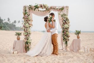 Ein Hochzeitspaar küsst sich unter einem Traubogen am Strand