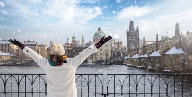Eine Frau steht vor einem Zaun an einem Fluss, der durch eine Stadt fließt, während es schneit