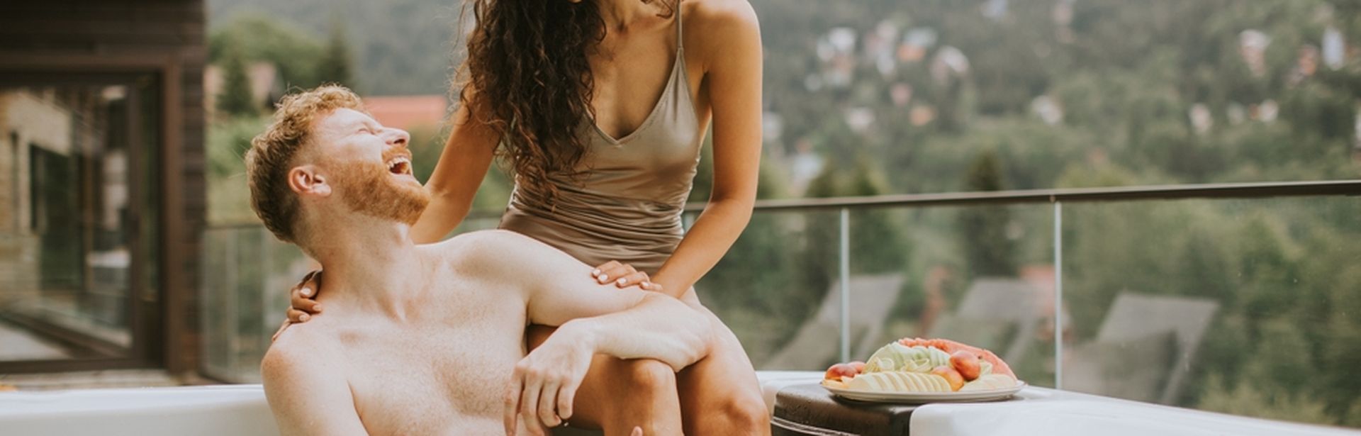 Ein Mann sitzt im Whirlpool und eine Frau sitzt hinter ihm auf dem Rand des Whirlpools