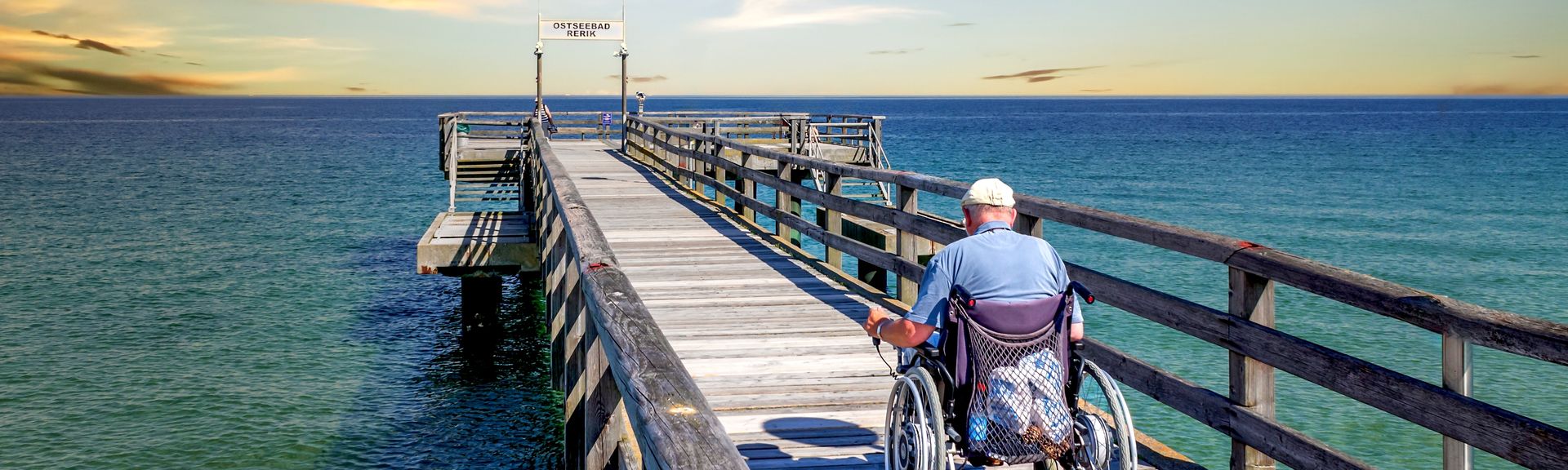 Mann im Rollstuhl auf einer Seebrücke am Meer