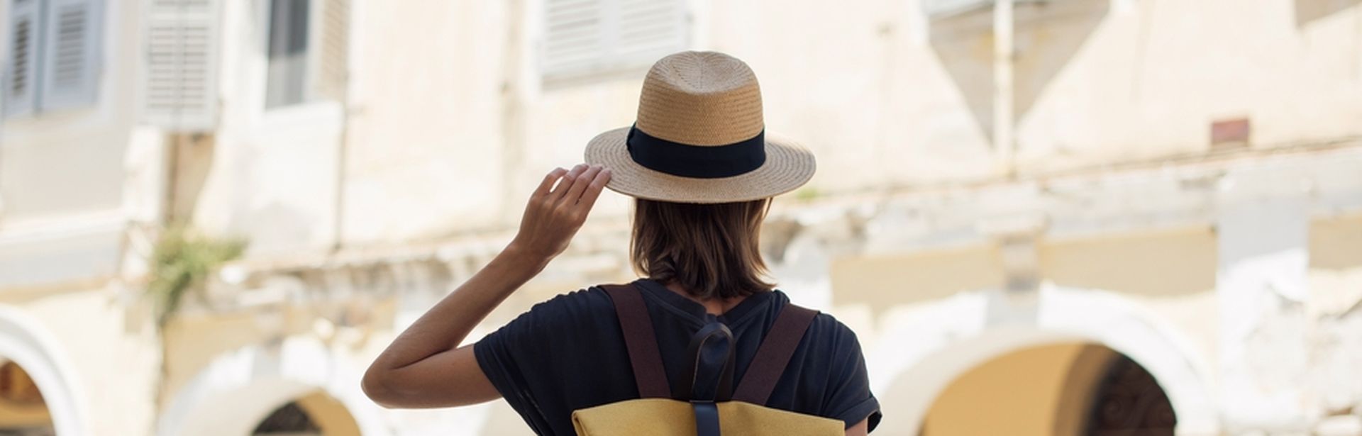 Eine Frau mit Hut und Rucksack schaut auf gelbe Gebäude in einer Stadt