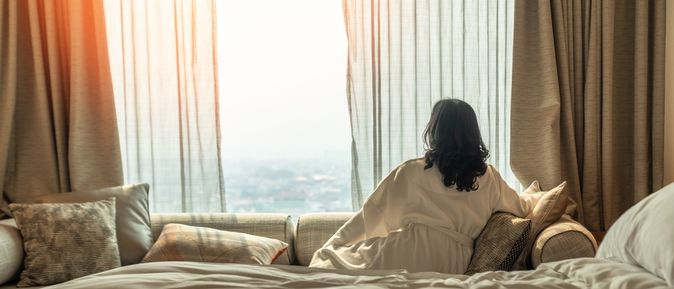 Eine Frau im Bademantel sitzt in einem Hotelzimmer auf dem Sofa und schaut aus den Fenster