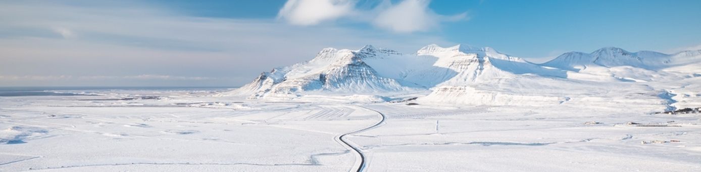 Weg durch eine flache Schneelandschaft mit Bergen im Hintergrund