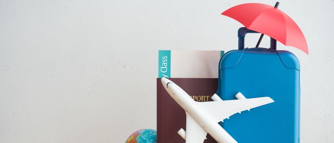 Ein Spielzeugkoffer, ein Spielzeugsonnenschirm, ein Spielzeugflugzeug, ein Reisepass und eine kleine Weltkugel stehen auf einem Tisch