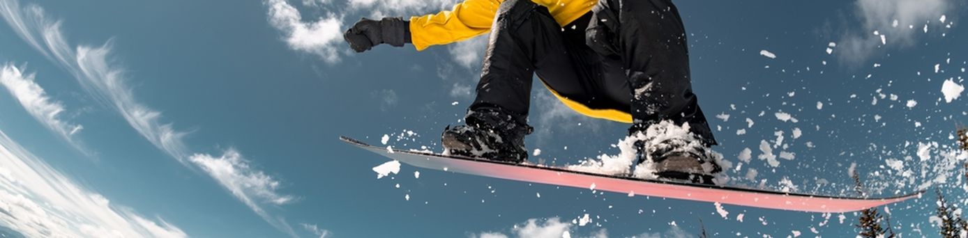 Eine Person in gelber Winterjacke springt mit einem Snowboard durch die Luft