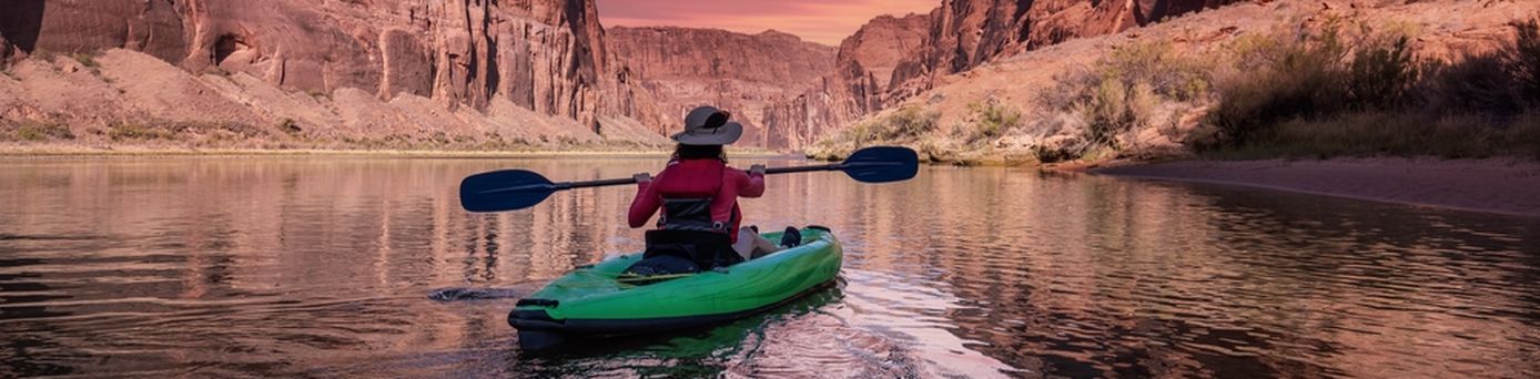 Eine Person sitzt in einem Grünen Kanu und schaut auf einen pinken Sonnenauf/untergang