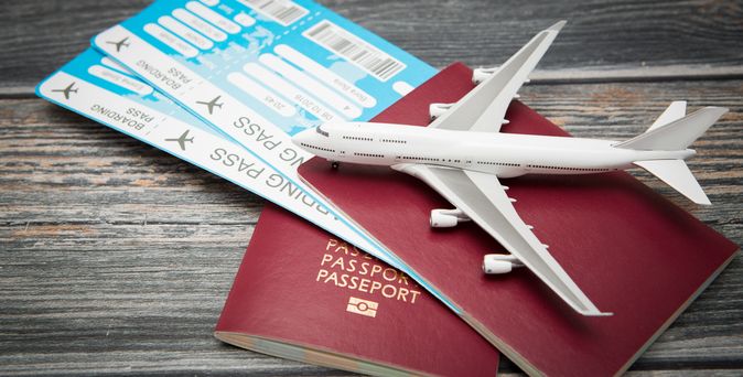 Zwei rote Reisepässe und zwei Flugtickets liegen auf einem Holztisch. Darauf liegt ein Miniaturflugzeug