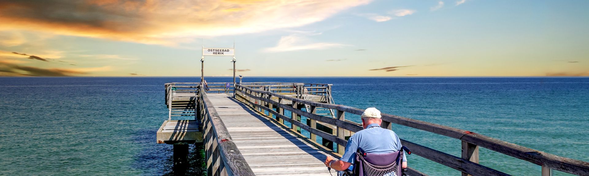 Mann im Rollstuhl auf einer Seebrücke am Meer