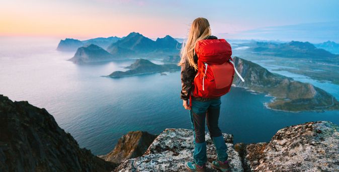 Alleinreisende Frau mit Rucksack schaut von einem Berg auf Wasser 