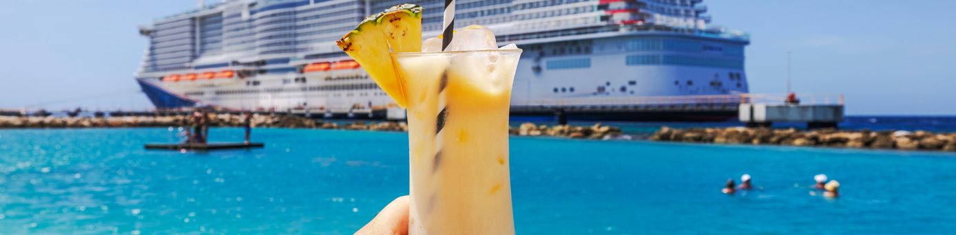 Eine Hand hält einen Cocktail hoch, im Hintergrund ist ein großes Kreuzfahrtschiff