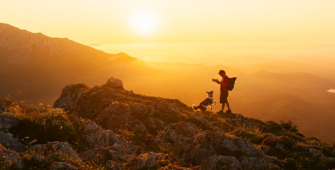 Mann und Hund wandern zusammen in den Bergen bei Sonnenuntergang