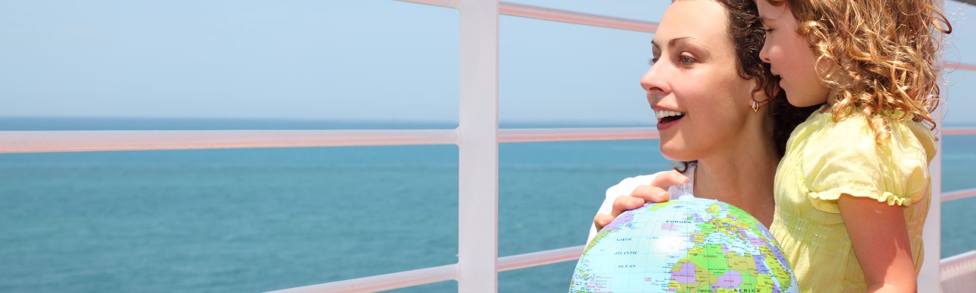 Mutter und Kind schauen über das Geländer eines Kreuzfahrtschiffes und halten einen Globus