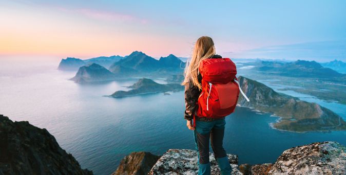 Alleinreisende Frau mit Rucksack schaut von einem Berg auf Wasser 
