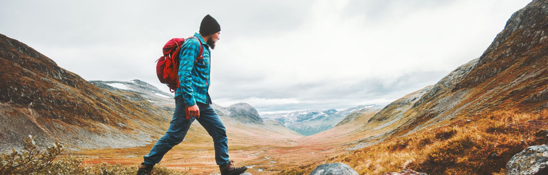 Ein Mann in Wanderkleidung läuft in einer Berglandschaft über Steine in einem Bach