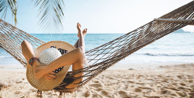 Frau mit Sonnenhut entspannt in einer Hängematte am Strand