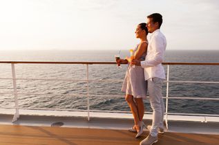 Ein Paar steht auf einem Kreuzfahrtschiff an der Reling und schaut aufs Meer