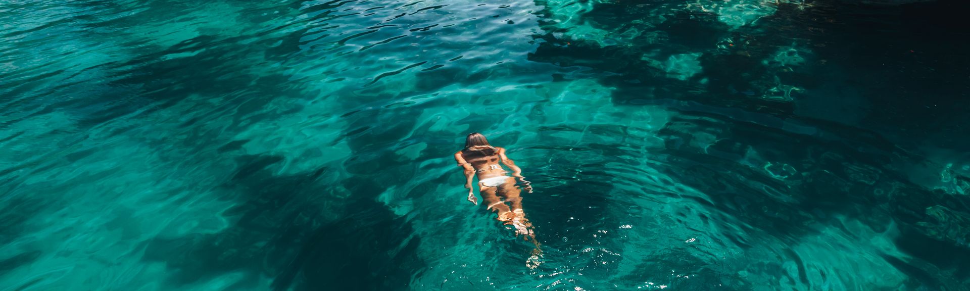Frau schwimmt im Meer umgeben von Felsen