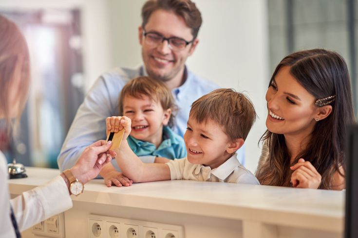 Eine Familie mit zwei Kindern beim Check-In, die Rezeptionistin reicht dem kleinen Kind die Zimmerkarte