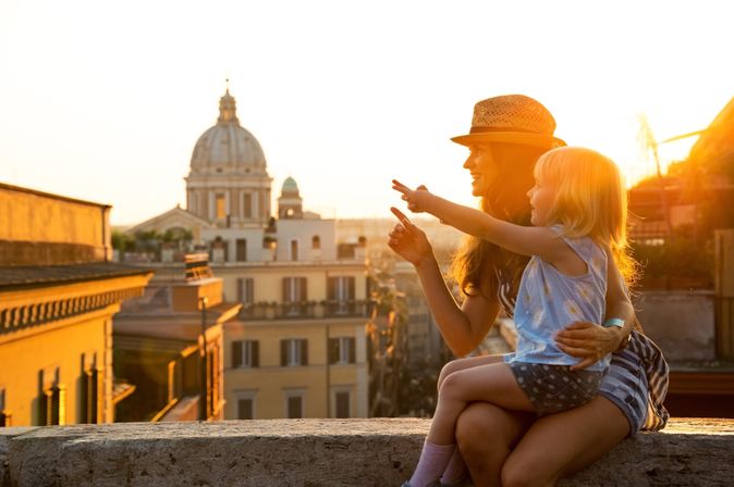 Eine Mutter und ein Kind sitzen auf einer Mauer und schauen sich eine Stadt bei Sonnenuntergang an