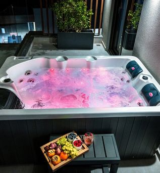 Whirlpool mit roter Beleuchtung im Wasser vor dem ein Tablet mit Obst und ein Getränk auf einem kleinen Tisch steht