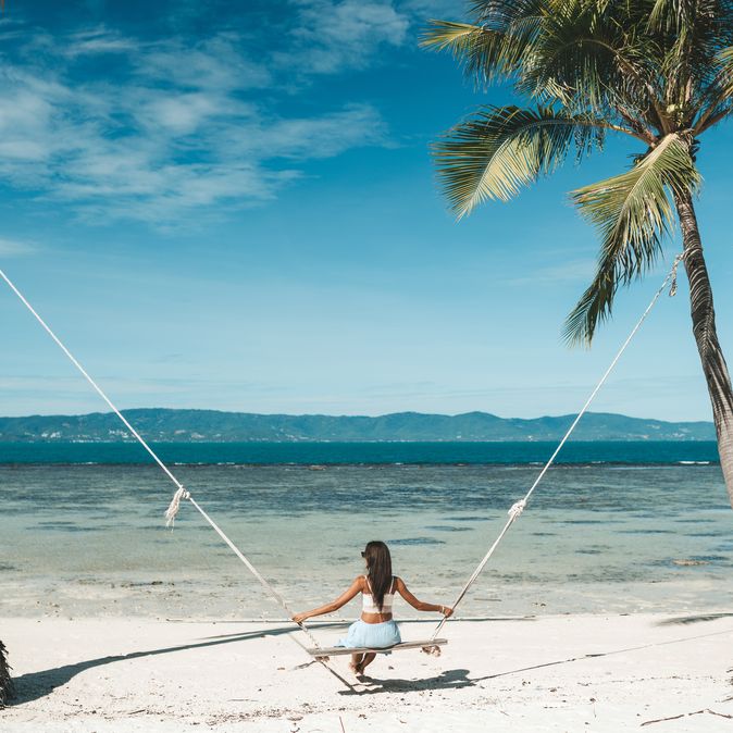 Frau auf einer Schaukel zwischen zwei Palmen am Meer