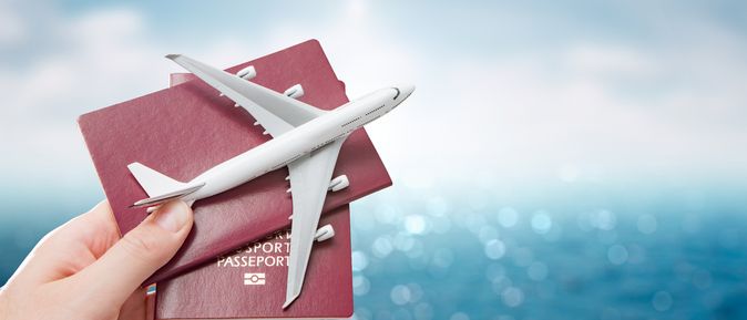 Eine Hand hält vor einem blauen Hintergrund zwei Reisepässe und ein Miniaturflugzeug hoch