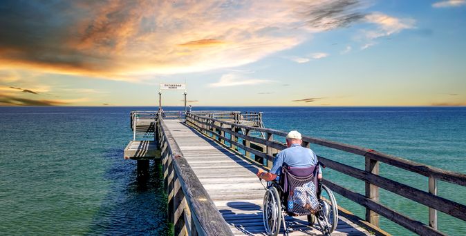 Mann im Rollstuhl auf einer Seebrücke am Meer
