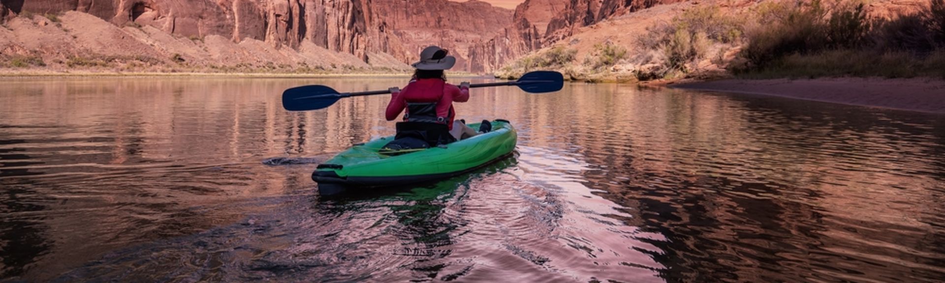 Eine Person sitzt in einem Grünen Kanu und schaut auf einen pinken Sonnenauf/untergang