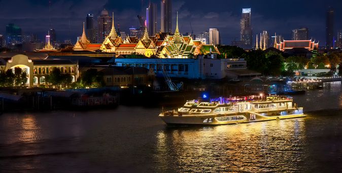 Flusskreuzfahrtschiff bei Nacht, das durch eine Stadt fährt
