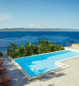 Ein Privatpool über dem Meer, um ihn herum einige Holzliegen und Bäume