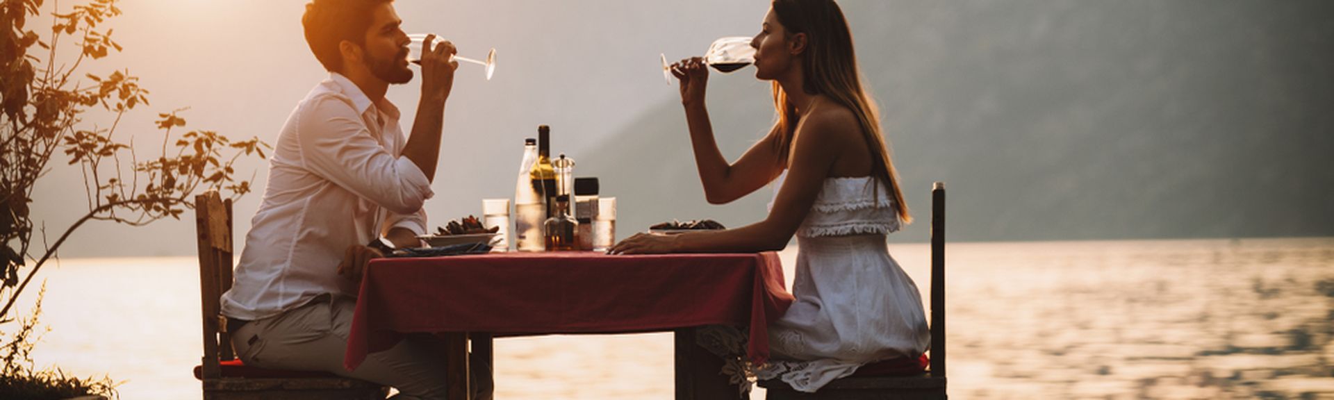 Eine Frau und ein Mann sitzen an einem Tisch am Wasser und trinken Wein