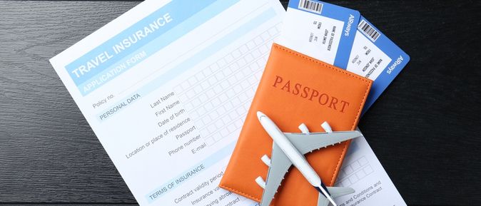 Ein Blatt Papier mit der Aufschrift "Travel Insurance Application Form" liegt mit einem Reisepass, zwei Flugtickets und einem kleinen Flugzeug auf einem Tisch