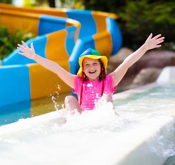 Ein glücklich aussehendes Kind rutscht durch eine Wasserrutsche und hebt die Arme