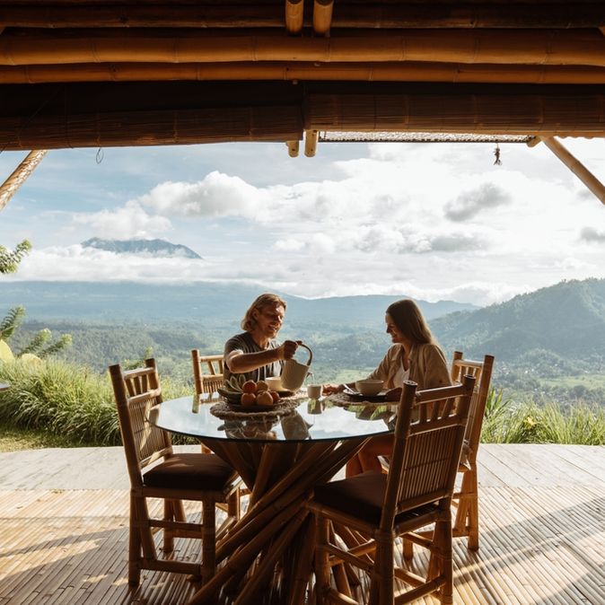Auf einer Terrasse mit beeindruckendem Ausblick auf eine grüne Landschaft sitzen zwei Personen an einem Tisch 