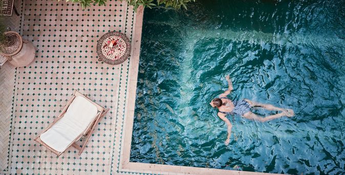Frau schwimmt in einem Pool; Neben dem Pool, auf der Terrasse steht eine Liege