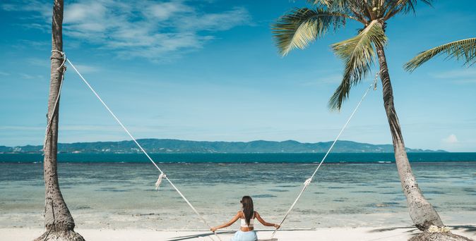 Frau auf einer Schaukel zwischen zwei Palmen am Meer